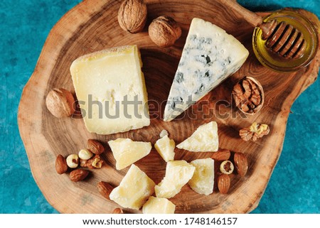 Cheese plate with a variety of cheeses, nuts, honey on a wooden board made of cut wood. On a blue textured background. Appetizer, aperitif, snack table
