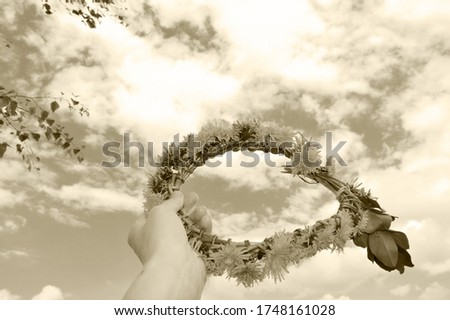 close-up - in a female hand a wreath of yellow dandelions, against the blue sky, white clouds and foliage of trees in black and white style