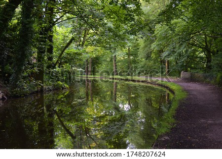 Canal and towpath going round a corner, with trees overhead and reflections in the water.