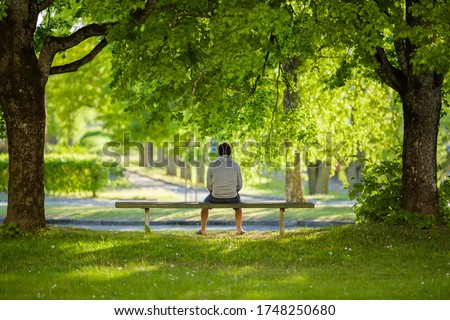 Young man sitting alone on bench between trees at beautiful green park. Thinking about life. Spending time alone in nature. Peaceful atmosphere. Back view.  Royalty-Free Stock Photo #1748250680