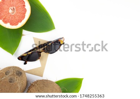 Coconuts, grapefruit, starfish, green tropical leaves, envelope and letter, sunglasses flat lay on white background with copy space. Summer, holidays, vacation, travel concept layout. Stock photo.