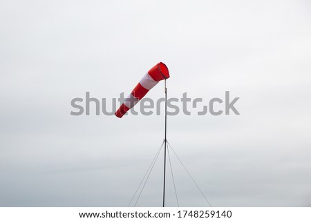 Frayed windsock in moderate wind against blue sky. Windsock flag with red and white stripes on blue sky background. Wind speed meter.