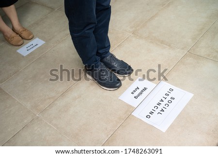 Close up of isolated shoes and legs of one person on  marking sign on the floor waiting and keeping distance while queueing at shop entrance in corona crisis