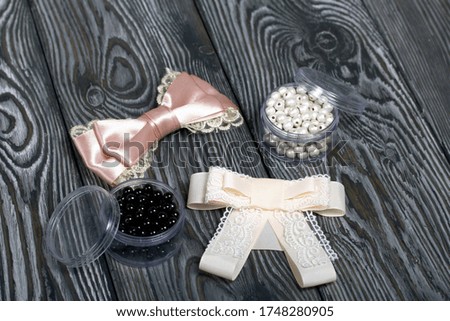 Hair clip made of pink ribbon. Jars with beads. On pine boards painted black and white.