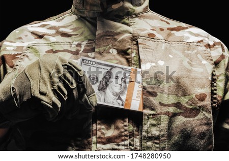 Photo of a soldier in camouflage and tactical gloves putting money in pocket. Royalty-Free Stock Photo #1748280950