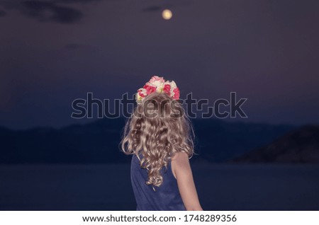 child with long blond curly hair looking to the full moon at night time