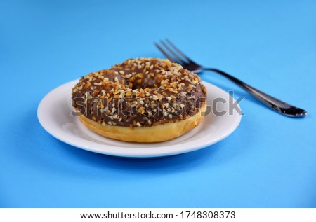 Chocolate donut on a plate stock images. Donut isolated on a blue background. Doughnut with chocolate frosting and nuts stock images