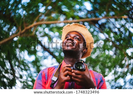 Happy african man traveler on vacation photographing with a dslr camera on the green nature background