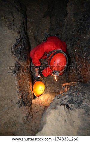 Caver in overalls in a narrow cave. Rescue from a narrow place of a stone cave. Historic mining light. Cave rescue. Spelunking, extreme sport. Caver performs out of a cave. Royalty-Free Stock Photo #1748331266