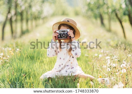 girl child with a camera sitting in nature. Little girl taking photos with a vintage camera.