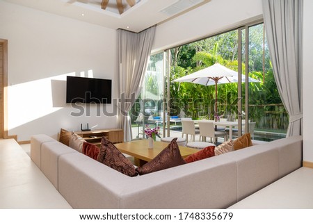 Interior and exterior design of living room with pool view in luxury pool villa feature television, sofa, couch, cushion, TV console, curtain and sliding door and garden Royalty-Free Stock Photo #1748335679