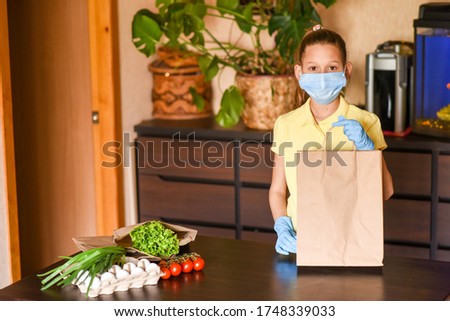  Woman with face mask on quarantine, cooks in the kitchen at home during coronavirus crisis. Stay at home. Enjoy cooking at home. Family concept. Beautiful girl brought vegetables and cooks.