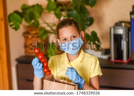  Woman with face mask on quarantine, cooks in the kitchen at home during coronavirus crisis. Stay at home. Enjoy cooking at home. Family concept. Beautiful girl brought vegetables and cooks.