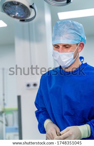 Portrait of male surgeon wearing surgical mask in operation theater at hospital. Modern equipment in operating room.