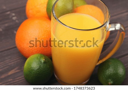 Freshly squeezed orange juice with three oranges and four limes on wooden table with space for text