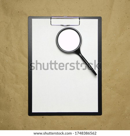 A tablet with a white sheet of A4 format with magnifier on a beige craft paper. Concept of analysis, study, attentive work. Stock photo with empty place for your text and design.