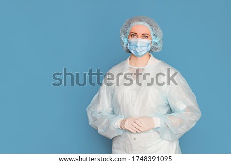 The doctor in a dressing gown, in medical gloves and masks. Surgeon with clinical experience in healthcare, patient care. Copy space, isolated blue background. Royalty-Free Stock Photo #1748391095