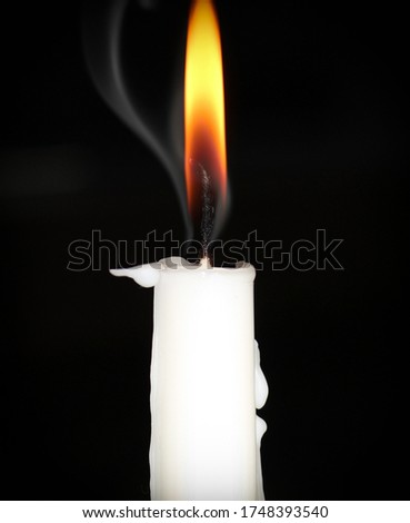 A burning white taper candle in front of a black background.