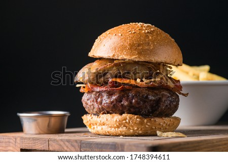 Beautiful and succulent beef burger made of prime beef with crispy bacon and fried onion rings lay on a wooden plate in sesame bread