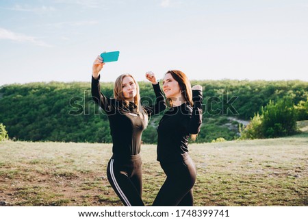 Girls in black tracksuits take selfies on a smartphone. Girls actively relax in nature.