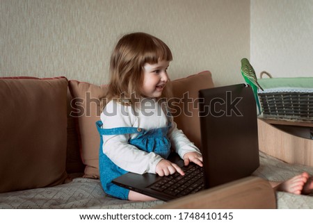 Beautiful little girl sitting on couch in living room and using laptop computer.Online training, games and watching cartoons. New generation. bright room