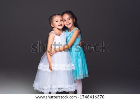 Two amazing hugging child girls. Smile and happiness. Perfect sisters in beautiful dresses at grey background