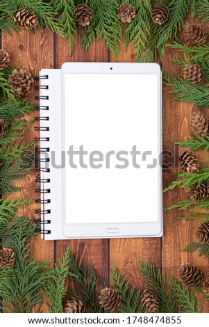 Top view of Wooden business table with Christmas decoration including blank mockup screen, pine branches and pine cones, Merry Christmas and happy new year concept, flat lay with copy space for text