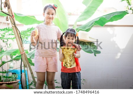 Close-up view of two lovely girls eating snacks (fried durian) while staying in the house during the summer break.