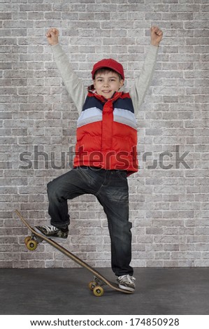 Skater boy crouching on his skateboard in front of brick wall. 