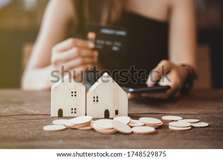 Hold a smartphone and a credit card and have a picture of a replica home on the front. Credit card concept.  Focus on a simulated wooden house. smartphone and a credit card. Photo noise and grains