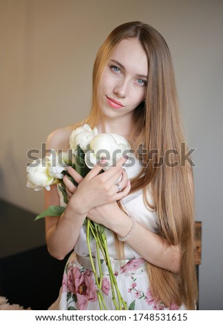 a girl with long light brown hair holds beautiful white peonies in her hands.