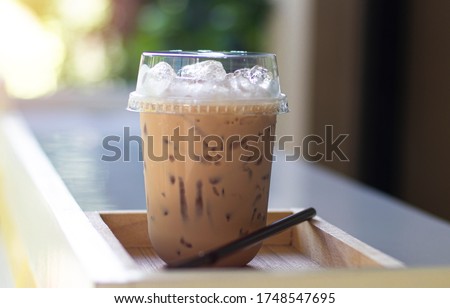 Iced milk tea in plastic glass, put on the wooden floor, behind it is a green garden. Royalty-Free Stock Photo #1748547695