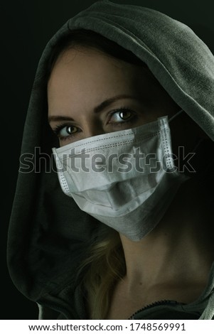 Dark photo of Young serious riot woman wearing medical protactive face mask and hood in the night