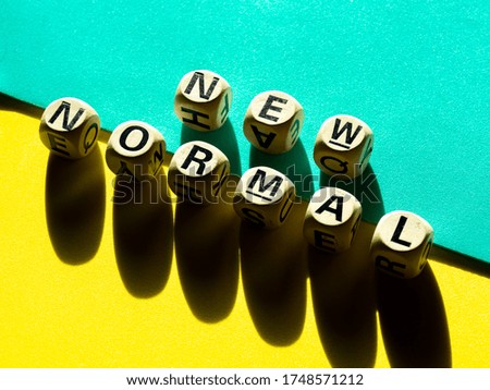NEW NORMAL, word on wooden alphabet cube on light green and yellow background, top view, minimal style. New normal after covid-19 pandemic with social distancing concept.