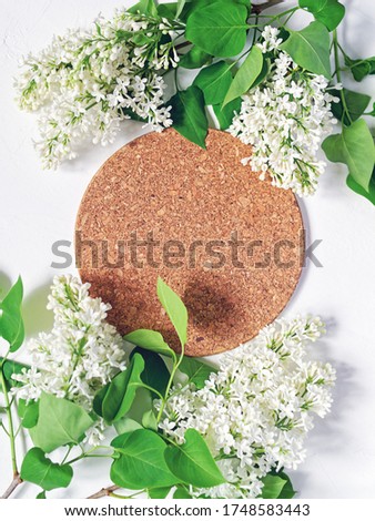 A circle of cork and a branch of white blooming lilac are on a white textural background. Spring-summer flower arrangement. Flat lay. Copy space. Vertical image.