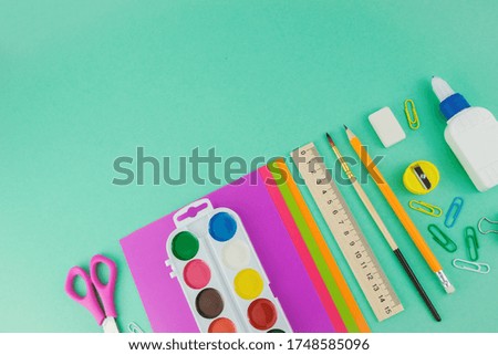 School supplies, top view of scissors, paper, watercolour paintings, brush, pen and ruler on the green background