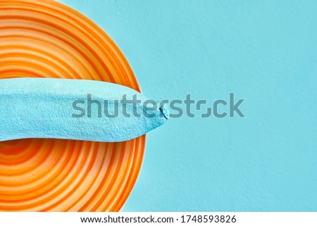 fragment of a colored blue banana on an orange plate. blue background. concept. creative. color matching. copys pace