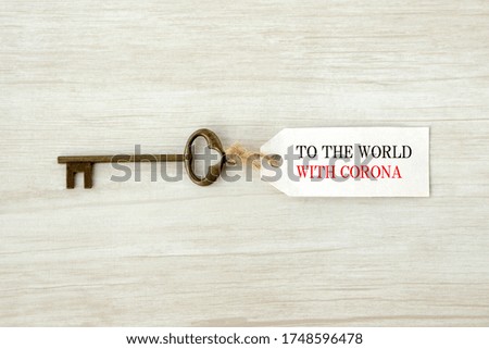 Key with tag "to the world with corona" words printed on white wooden board