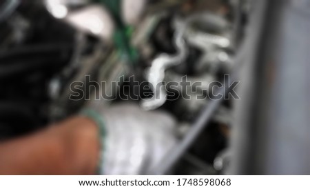 Friendly and competent auto mobile mechanic in a workshop repairs a car. Blurry background