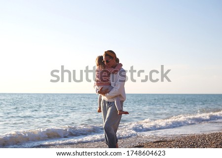 mom and daughter hug and kiss on the beach at sunset.