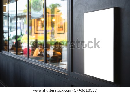 Mockup blank white screen outdoor advertise lightbox mounted on the black wall of a building with blurred restaurant background.