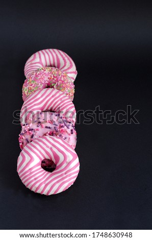 Donuts with pink icing are lying next to each other on a black background. Vertical background, selective focus.