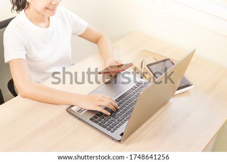 Crop image of asian woman in glasses working on laptop and using smartphone. Young woman with notebook and laptop computer working on wood table. Work and study from home concept.