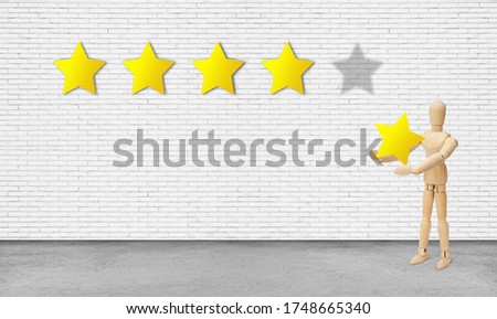 Customer Feedback Concept : Wooden figure model holding and giving yellow star for best service ranking on white brick wall.
