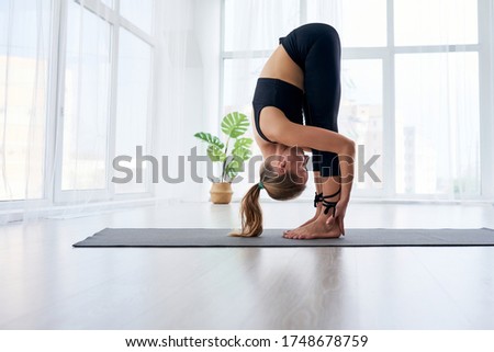 young beautiful woman doing yoga in a modern bright room with large windows at sunny day. Yoga at home concept. Royalty-Free Stock Photo #1748678759