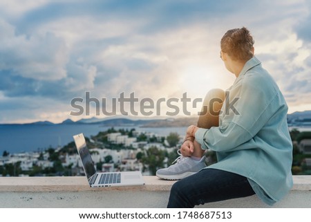 Female businesswoman girl in eyeglasses working on laptop in early morning with city panorama in background