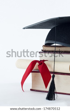 A graduation mortarboard on top of a stack of books, with parchment scroll tied in red ribbon. Royalty-Free Stock Photo #174870512