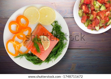 red fish trout fillets on white plate with vegetable salad top view. fish trout on purple wooden background. trout with dill, lemon and pepper