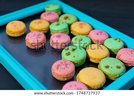 Macaroons of multiple flavors and colours: pink macaroons with strawberry, green with kiwi and beige macaroons with peaches filled with tasty whipped cream in a light blue frame on a dark background