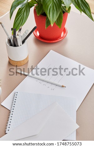 green plant, envelope, blank notebook, pencils and pens and paper with plan lettering on beige surface